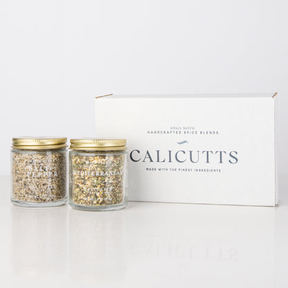 two jars of gold and silver grains next to a white box