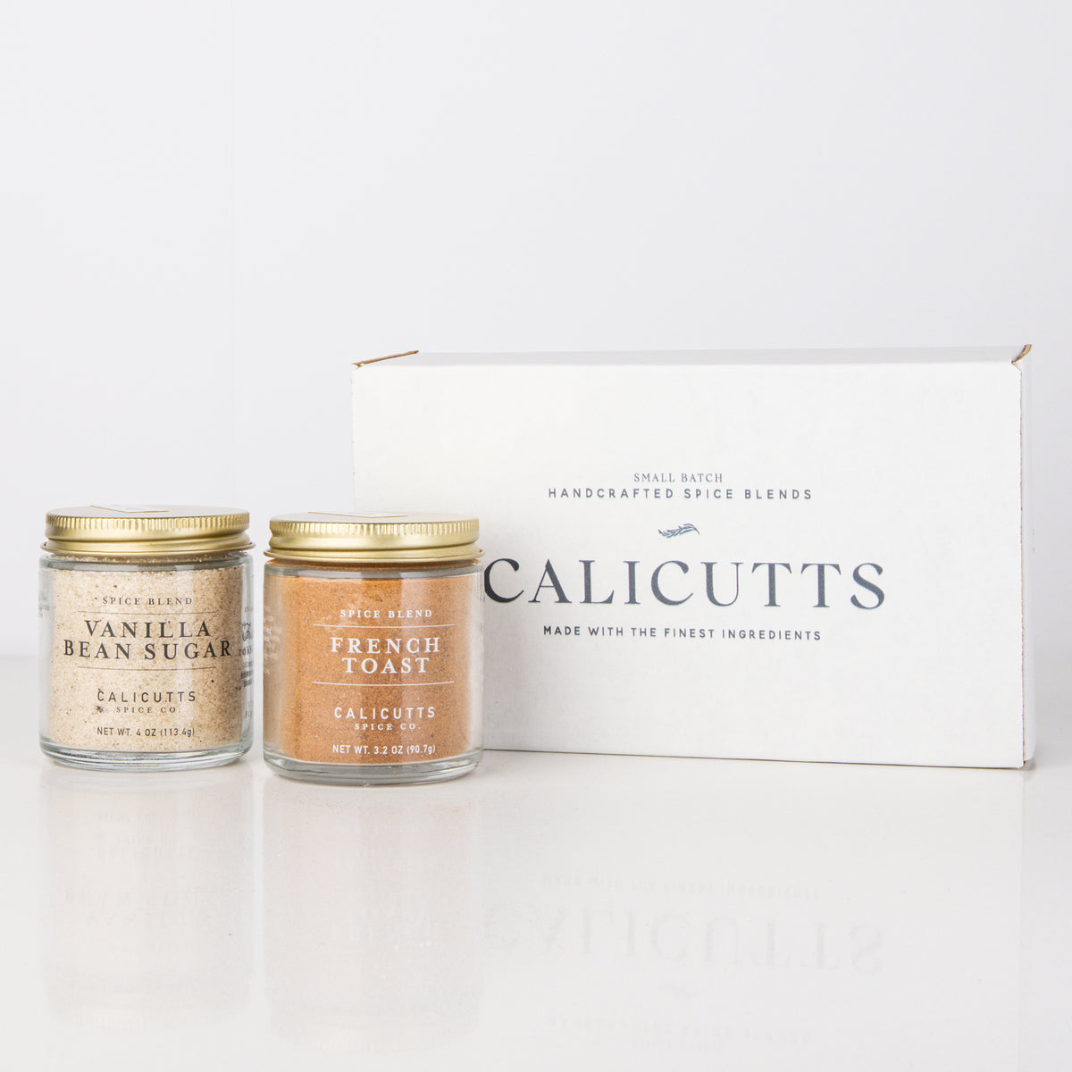 a couple of small jars with gold caps next to a white box